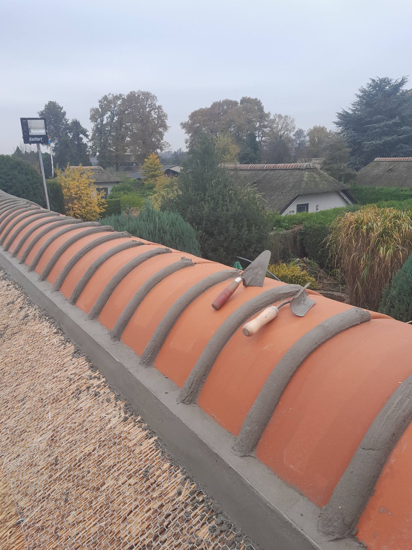 Nok van een rieten dak met oranje vorsten in de specie, troffels erop