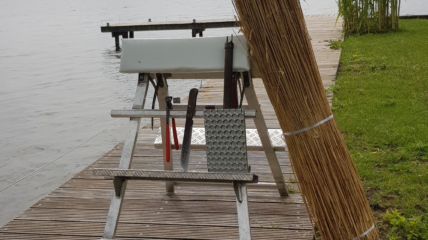 Werkbank met gereedschap op een steiger aan het water, met een bos riet ernaast