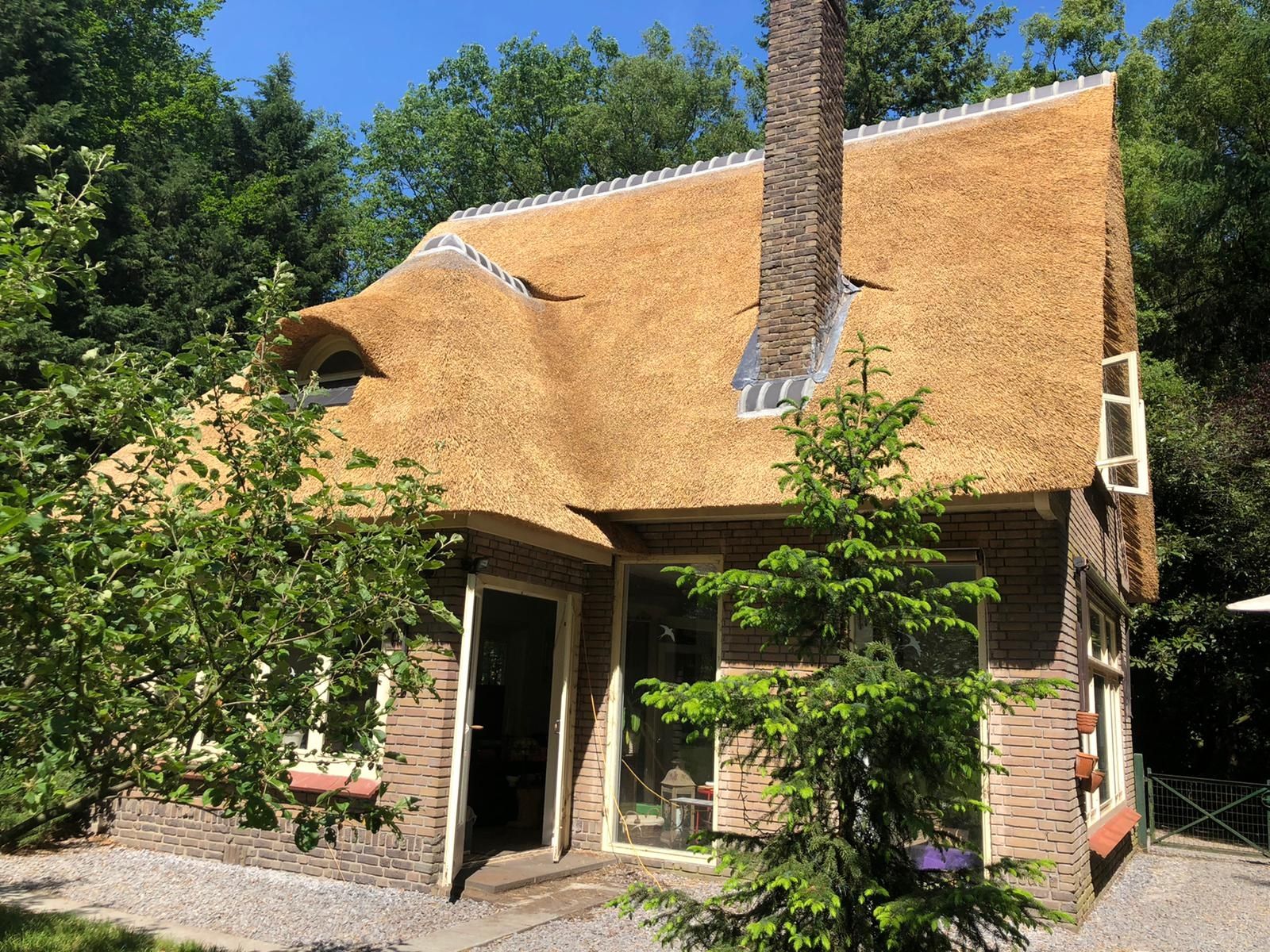Woning met een rieten dak dat in een golf om de schoorsteen loopt